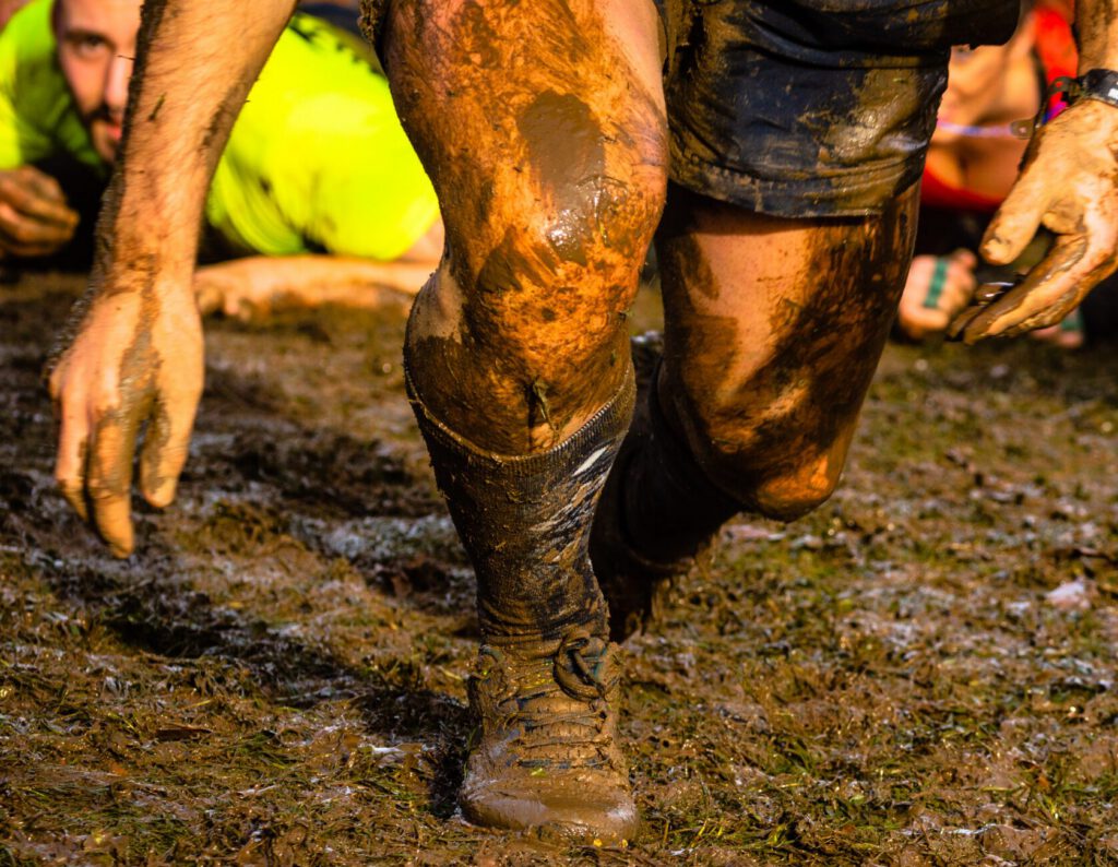 Mud race runners passing under a barbed wire obstacles during extreme obstacle race,detail of legs