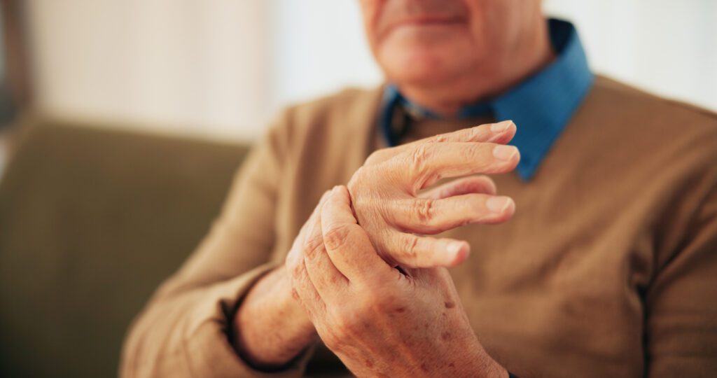Home, hands and senior man with wrist pain, arthritis and inflammation with carpal tunnel syndrome. Closeup, pensioner or elderly person with osteoporosis, fibromyalgia or parkinson disease in lounge